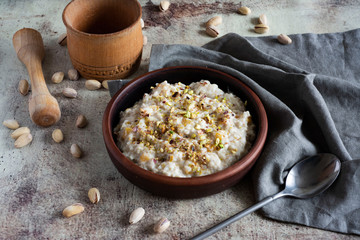 Delicious oatmeal porridge with pumpkin slices and nuts in a stylish clay plate on a gray background