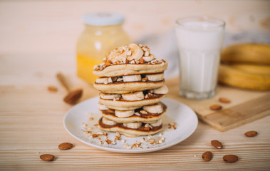 Stack of delicious pancakes with honey, nuts and slices of banana.