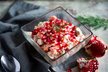 Healthy meat salad with pomegranate seeds in a glass salad bowl on a gray napkin, pomegranate seeds randomly scattered on a gray background