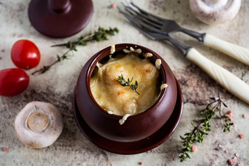 Delicious julienne with mushrooms, chicken, Parmesan and thyme in a clay pot, fresh tomatoes and fresh mushrooms randomly scattered on a gray background