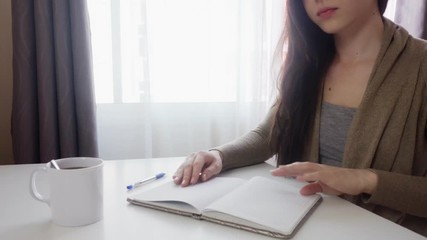 A young woman sits at a table and writes notes in a notebook. A list of important tasks for the week. Close-up