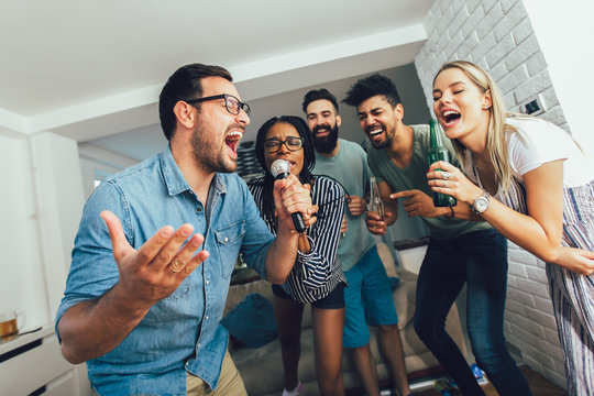 Happy friends singing together at home. Karaoke party concept