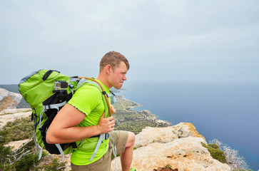 A tourist on a mountain with a backpack looks into the distance.