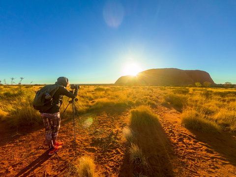 Uluru Ayers Rock photographer silhouette at sunrise. Photographer woman taking pictures with tripod in Uluru-Kata Tjuta National Park. Sun rays in Australian outback. Northern Territory, Australia.