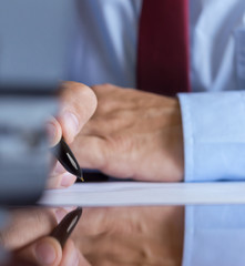 Man signing a document or writing correspondence with a close up view of his hand with the pen and...