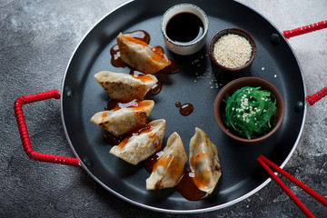 Serving pan with fried gyoza dumplings over dark-grey stone background, elevated view, studio shot