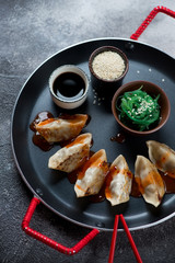 Gyoza dumplings with seaweed salad, sesame and soy sauce on a serving pan, vertical shot, close-up