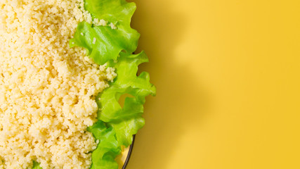 couscous porridge with lettuce and healthy fitness food on a yellow background. copy space