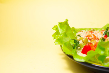 couscous porridge with lettuce and vegetables on a yellow plate on a yellow background healthy fitness food. copy space