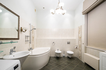 Fototapeta na wymiar Modern interior of bathroom in light tones with black tile on the floor. Bath, toilet and sink.