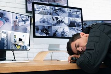 Male security guard sleeping near monitors at workplace
