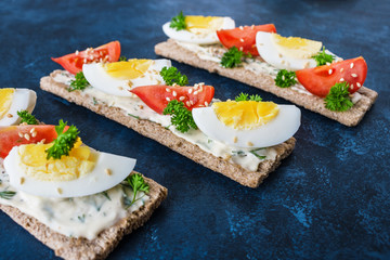 healthy sandwiches with crispbread soft cheese boiled eggs tomatoes sesame seeds on dark blue background close up