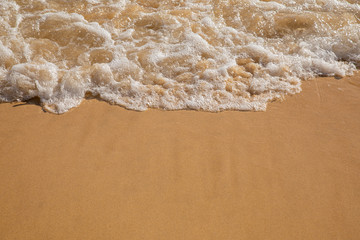 Fototapeta na wymiar Waves breaking on an empty sand beach and spalsh producing foam - travel holiday vacation summer sun - splashing water - wavy golden yellow sand background - empty space