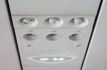Air vents and light switches over the top of the seat on the plane.