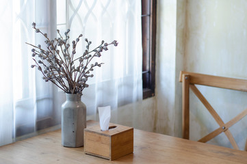 Dry flower vase And a tissue box on the table in the room. The light shines through the curtain from the window.