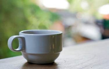 White hot coffee cup with smoke floating out Put on a wooden balcony With a blurred tree backdrop