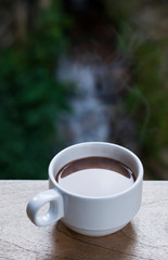 White hot coffee cup with smoke floating out Put on a wooden balcony With a blurred tree backdrop