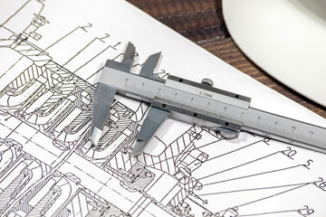 Some pump blueprints on a wooden desk with hardhat and calipers.