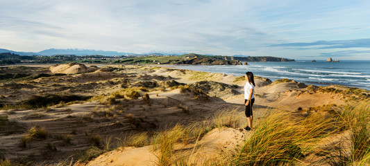 Young woman in sport dress standing on the stone, looking at sunset over the sea