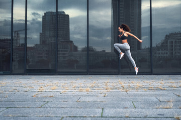 Fototapeta na wymiar Young athletic woman running in the city, shot of girl jumps on the glass building background