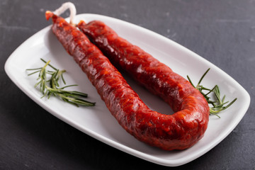 smoked sausage with rosemary on white dish on ceramic background