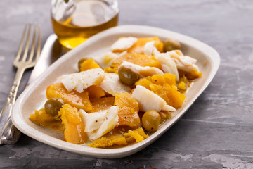 cod fish with sweet potato and olives on dish on ceramic background