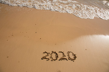 Summer beach holiday 2020 season golden sand - year - decade - new season lettering on the beach with wave and clear blue sea. Numbers 2020 year on the sea shore, message handwritten New Years concept