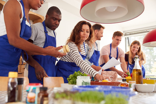 Male And Female Adult Students Looking At Recipe In Cookery Class In Kitchen