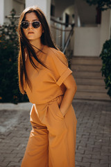 stylish young attractive woman wearing an orange-colored trouser suit and sunglasses photographed...