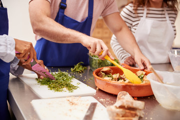 Close Up Of Male And Female Adult Students Preparing Ingredients For Dish In Kitchen Cookery Class
