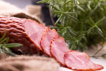 Krakowska dried sausage cut into slices on wood boards decorated with jute fabric and rosemary. Traditional cold cuts.
