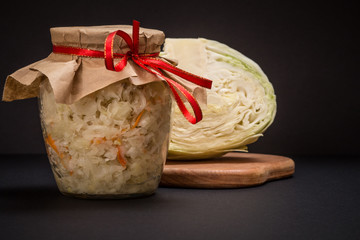 Fermented cabbage with herbs and spices in glass jar on the black background