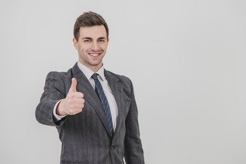 Handsome businessman standing, giving thumb up, smiling, showing his satisfaction.