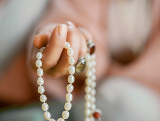 Hand with pearl rosary beads. Meditation accessory.
