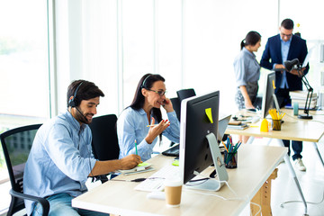Attractive business people in headsets are smiling while working with computer in modern office