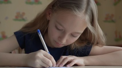 Cute smiling girl talking and writing with pen on paper at desk. Adorable cheerful teenage girl sitting at wooden table and writing on paper sheet at home