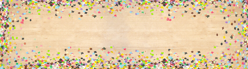 Carnival background panorama banner long - Frame made of colorful confetti isolated on brown wooden texture, top view with space for text