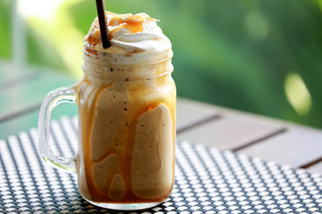 Closeup Iced Coffee Caramel Macchiato Frappe with whipping cream on top in the mug glass on wooden table background. Drink for summer concept.