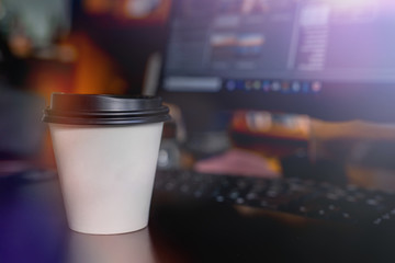 A cup of coffee takeaway on the desk with a monitor on background