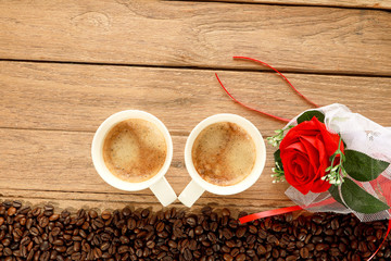 Top view shot of Two hot fresh coffee in a white cup with foam and coffee beans and red roses flowers on wooden table background. Drink or love and valentine concept. Warm tone.