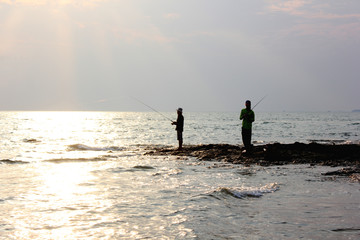Silhouette of man fishing on the beach at sunset.