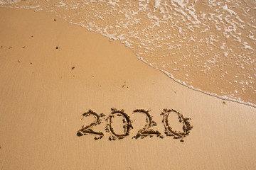Fototapeta premium Summer beach holiday 2020 season golden sand - year - decade - new season lettering on the beach with wave and clear blue sea. Numbers 2020 year on the sea shore, message handwritten New Years concept