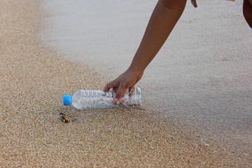 woman's hand collects plastic bottle on beach background. cleaning up beach. picking up plastic water bottle from the sandy beach. 