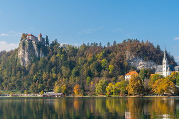 Fototapeta na wymiar View to beautiful lake Bled surrounded by trees and famous red roof castle on peak of hill on clear day. Travel landscapes and landmarks concept