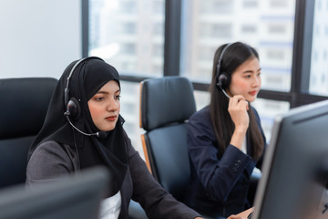 Arabian or Muslim woman works in a call center operator and customer service agent wearing microphone headsets working on computer in a call center, talking with customer