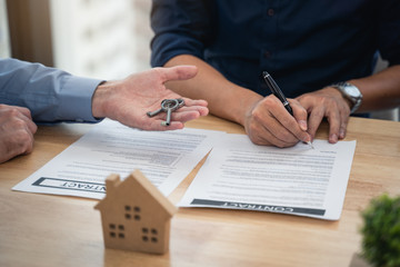 Asian young man signed contact home purchase or rental in office of estate agent and Sale representative giving key from new house to young couple in office