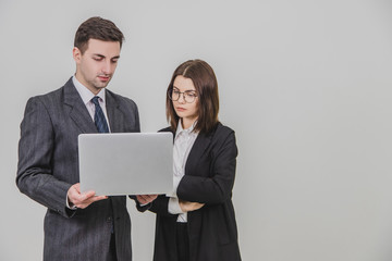 Business partners standing, checking data in the laptop. Woman is standing, her hands folded.