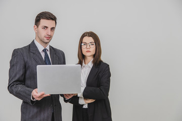 Business partners standing, checking data in the laptop. Woman is standing, her hands folded. Confident face expressions.