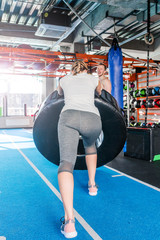 Fit female athlete working out with a huge tire, turning and flipping in the gym.