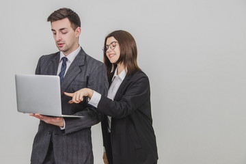 Handsome man standing, working with laptop. Woman is pointing from man's behind at something in the laptop, interfering him. Man is annoyed because of this.